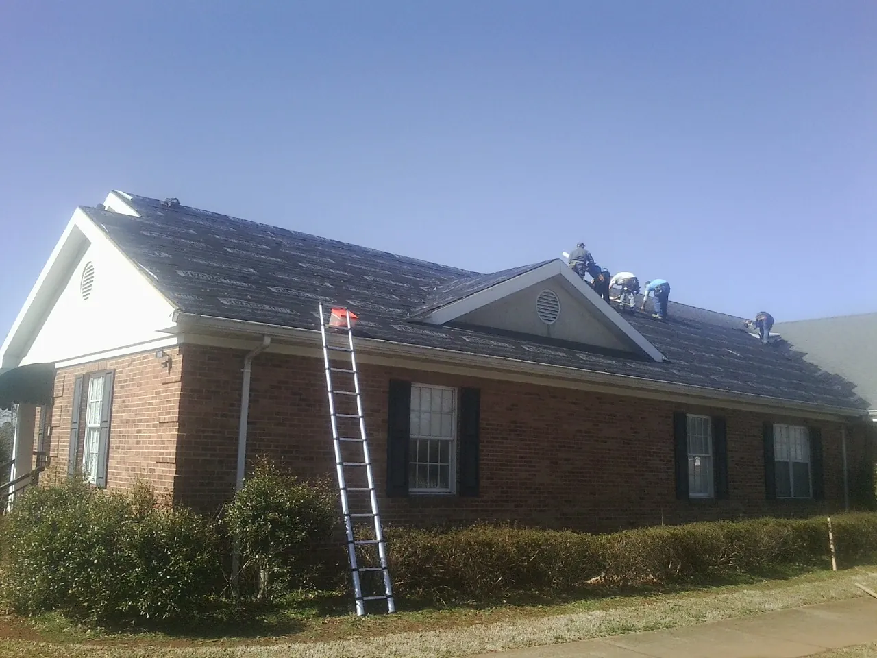 Crew tearing shingles off a brick ranch roof with a ladder set — Metal Roof Repair work by our crew in Estillfork
