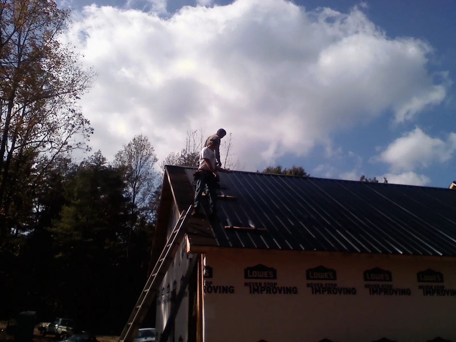 Roofer fastening dark metal panels high against a cloudy sky, from a Roof Inspection job in Estillfork